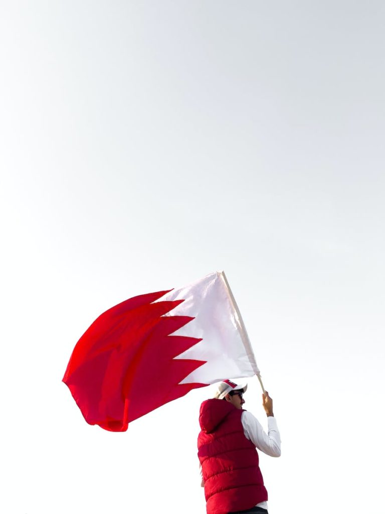 Man in White Longsleeve and Red Vest Holding a Flag of Bahrain