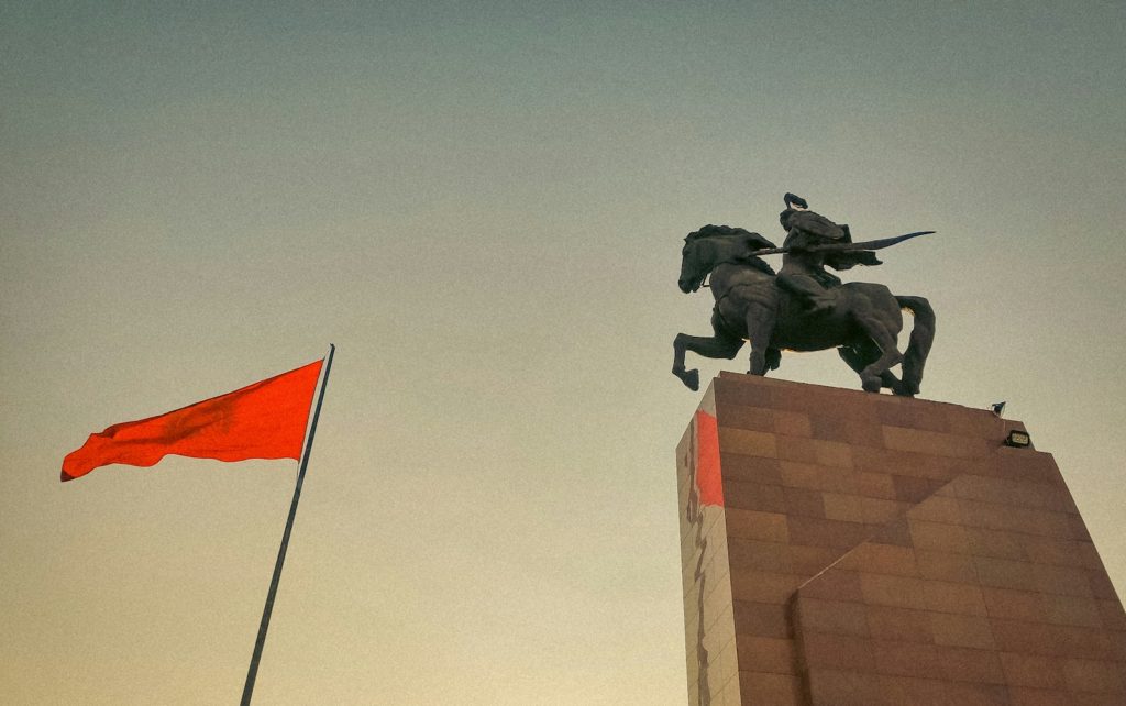 a statue of a man riding a horse next to a red flag